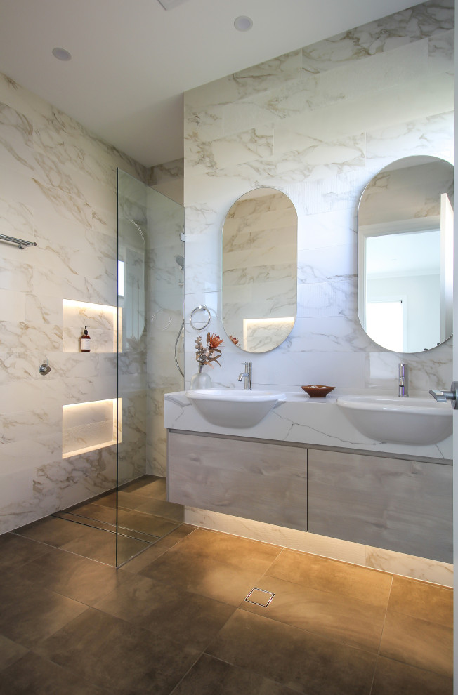 This is an example of a mid-sized contemporary master bathroom with flat-panel cabinets, light wood cabinets, an alcove shower, a one-piece toilet, porcelain tile, white walls, porcelain floors, engineered quartz benchtops, brown floor, an open shower, a niche, a double vanity, a floating vanity, multi-coloured tile, multi-coloured benchtops and a drop-in sink.