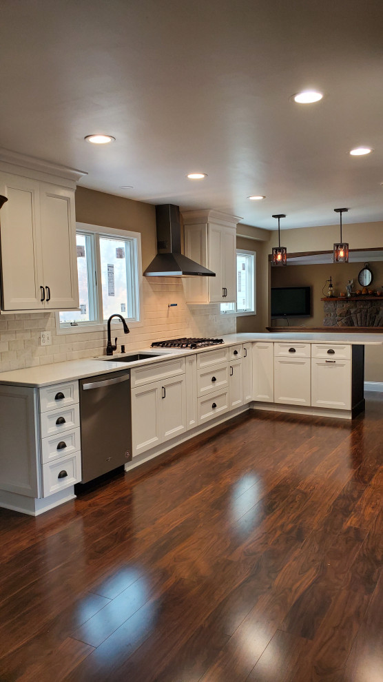 Mid-sized country l-shaped open plan kitchen in Philadelphia with an undermount sink, shaker cabinets, white cabinets, quartz benchtops, white splashback, stone tile splashback, stainless steel appliances, laminate floors, no island, brown floor and white benchtop.