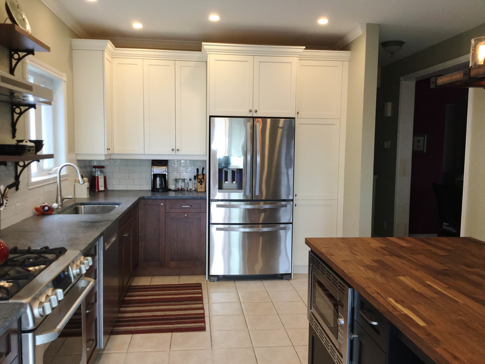 Inspiration for a mid-sized transitional l-shaped kitchen remodel in Ottawa with an undermount sink, shaker cabinets, dark wood cabinets, soapstone countertops, white backsplash, ceramic backsplash, stainless steel appliances and an island
