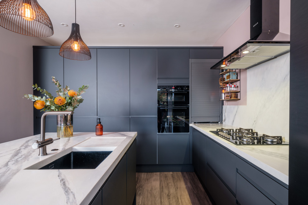 Immagine di una grande cucina moderna con lavello sottopiano, ante lisce, ante blu, paraspruzzi bianco, elettrodomestici neri, pavimento marrone e top bianco