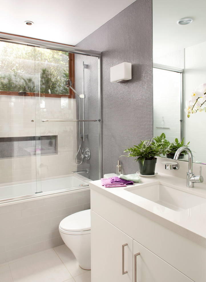 Mid-sized contemporary kids bathroom in San Francisco with mosaic tile, grey walls, a shower/bathtub combo, flat-panel cabinets, white cabinets, an alcove tub, a two-piece toilet, gray tile, porcelain floors, an undermount sink, engineered quartz benchtops, white floor and white benchtops.