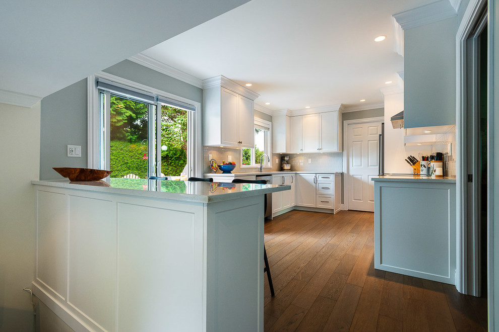 Example of a mid-sized transitional u-shaped medium tone wood floor and brown floor kitchen design with an undermount sink, shaker cabinets, white cabinets, quartz countertops, white backsplash, subway tile backsplash, stainless steel appliances, no island and white countertops