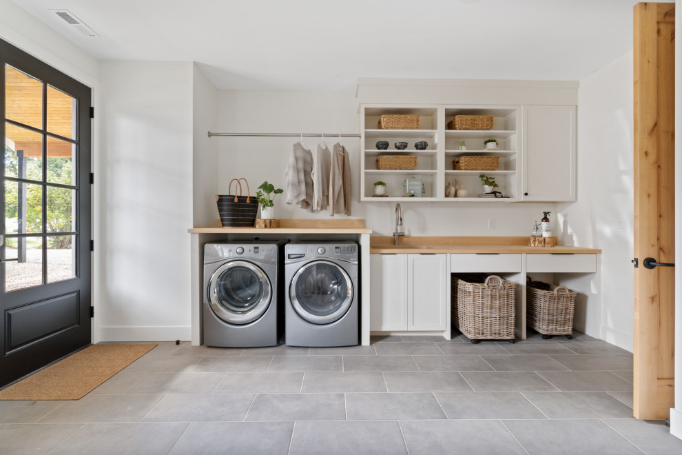 Large country single-wall utility room in Portland with a submerged sink, shaker cabinets, white cabinets, wood worktops, wood splashback, white walls, porcelain flooring, a side by side washer and dryer, grey floors and beige worktops.