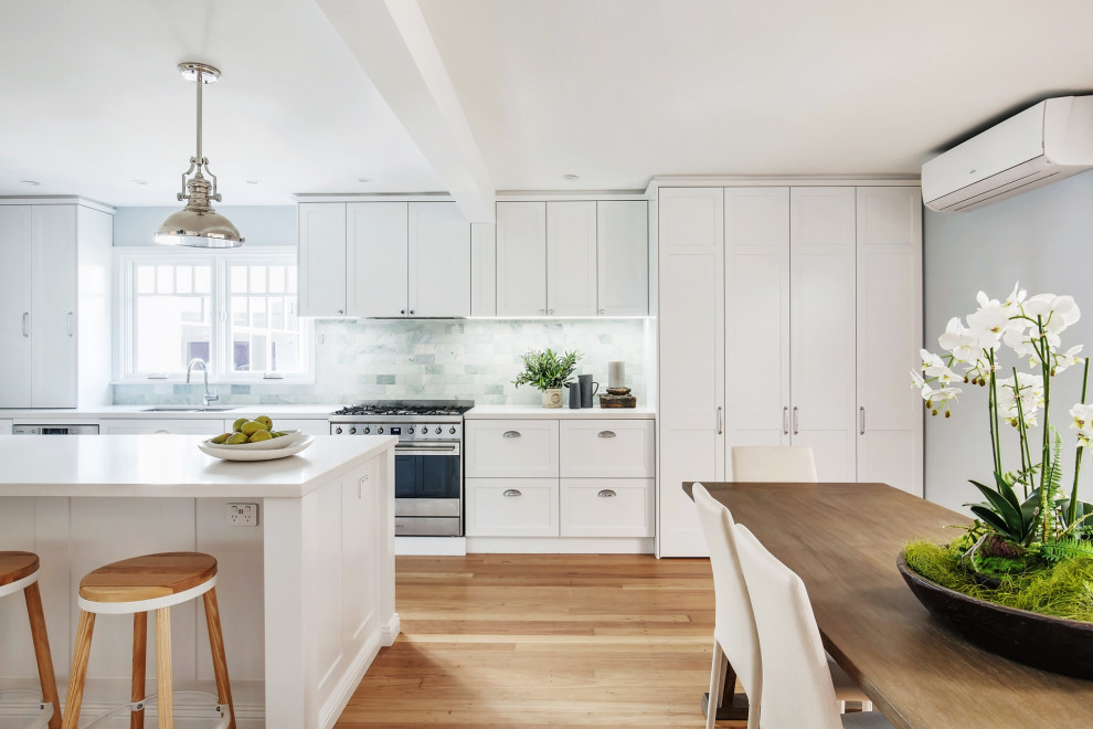 This is an example of a large modern single-wall open plan kitchen in Sydney with shaker cabinets, white cabinets, marble benchtops, green splashback, subway tile splashback, stainless steel appliances, medium hardwood floors, with island, brown floor and white benchtop.