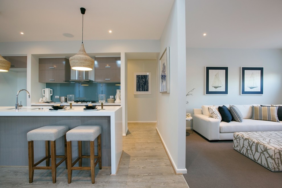 This is an example of a mid-sized beach style galley eat-in kitchen in Melbourne with an undermount sink, medium wood cabinets, solid surface benchtops, blue splashback, glass sheet splashback, stainless steel appliances, light hardwood floors, with island, brown floor, white benchtop and flat-panel cabinets.