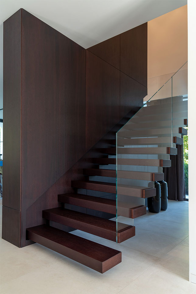 Immagine di una scala sospesa minimalista con pedata in legno, parapetto in vetro e pareti in legno