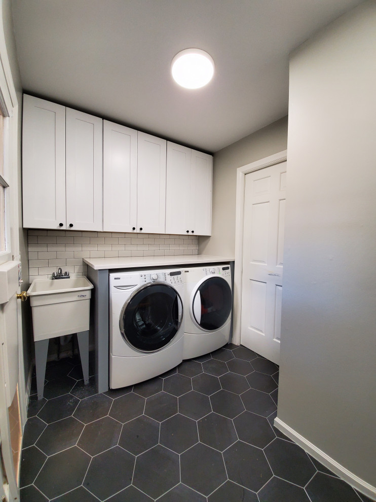 Design ideas for a mid-sized contemporary single-wall utility room in Chicago with an utility sink, shaker cabinets, white cabinets, quartz benchtops, grey walls, porcelain floors, a side-by-side washer and dryer, black floor and white benchtop.