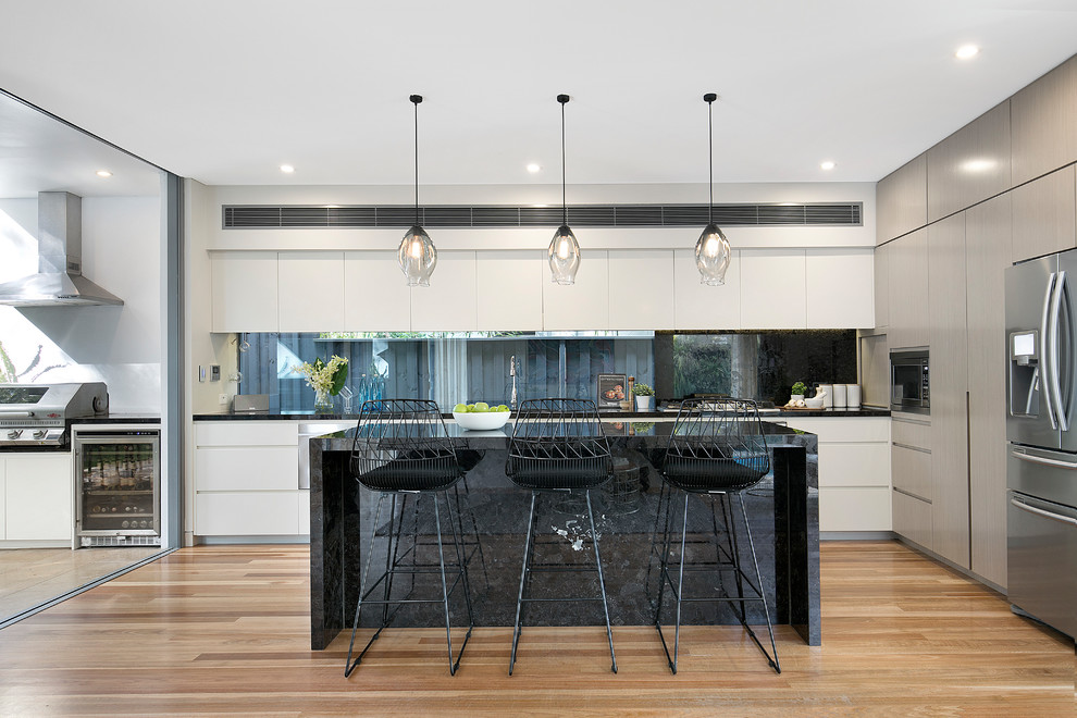 Inspiration for a mid-sized contemporary l-shaped kitchen in Sydney with window splashback, stainless steel appliances, medium hardwood floors, with island, black benchtop, flat-panel cabinets, white cabinets, an undermount sink, beige floor and marble benchtops.
