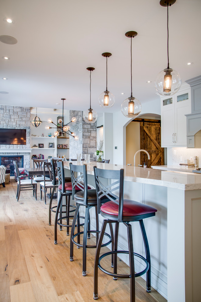 Example of a mid-sized transitional u-shaped light wood floor and brown floor eat-in kitchen design with an undermount sink, shaker cabinets, granite countertops, multicolored backsplash, stainless steel appliances, an island and white cabinets