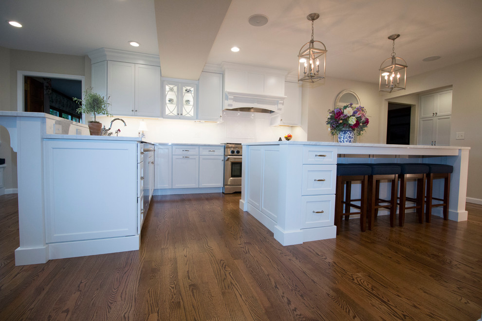 Huge transitional medium tone wood floor open concept kitchen photo with an undermount sink, shaker cabinets, white cabinets, marble countertops, white backsplash, ceramic backsplash, stainless steel appliances and two islands