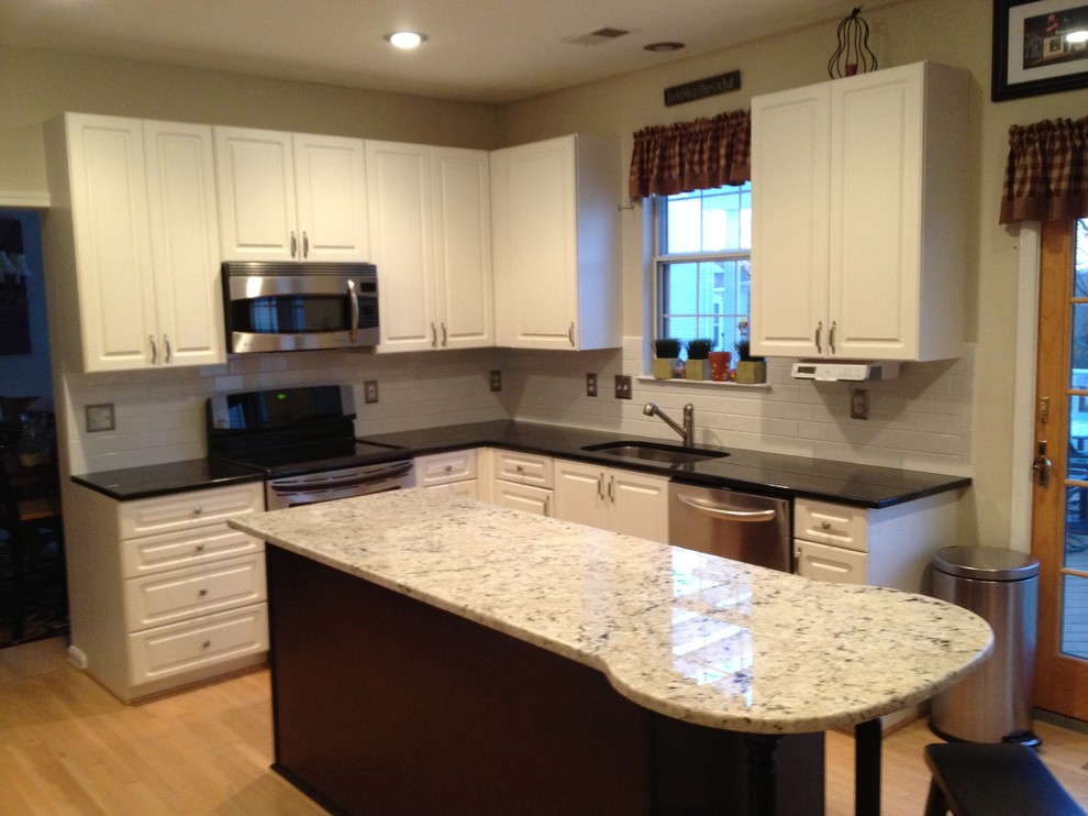 Example of a mid-sized trendy l-shaped light wood floor and brown floor kitchen design in DC Metro with a single-bowl sink, raised-panel cabinets, white cabinets, solid surface countertops, white backsplash, subway tile backsplash and an island
