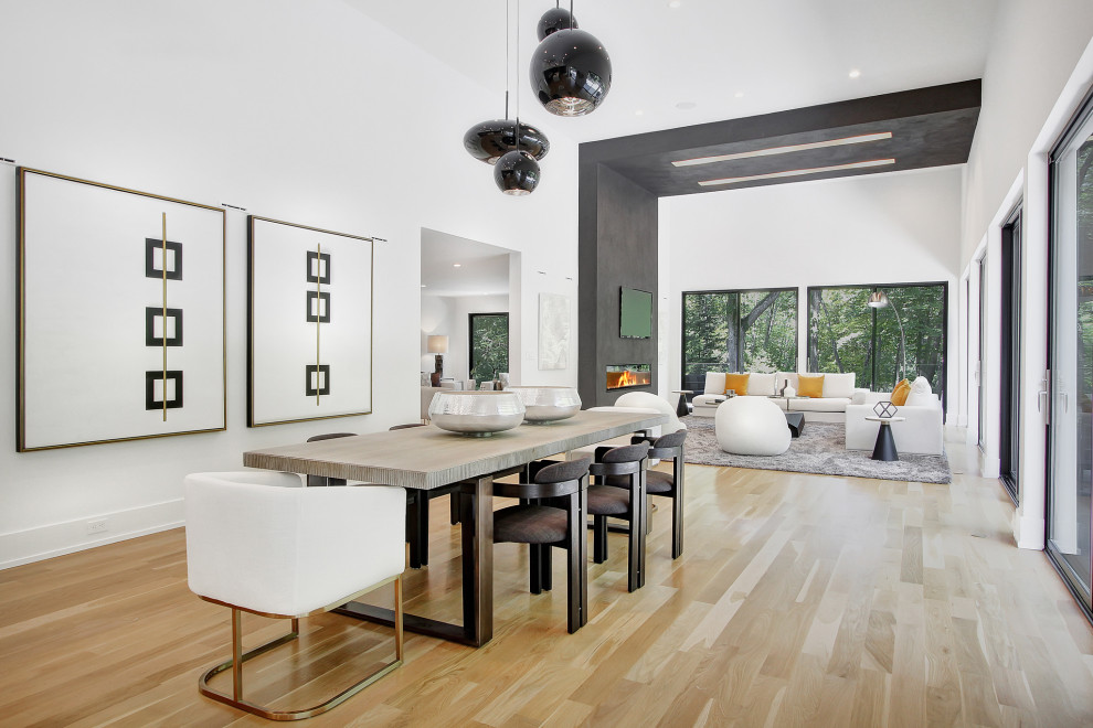 Photo of a large modern open plan dining in New York with white walls, light hardwood floors, a hanging fireplace, a concrete fireplace surround and vaulted.