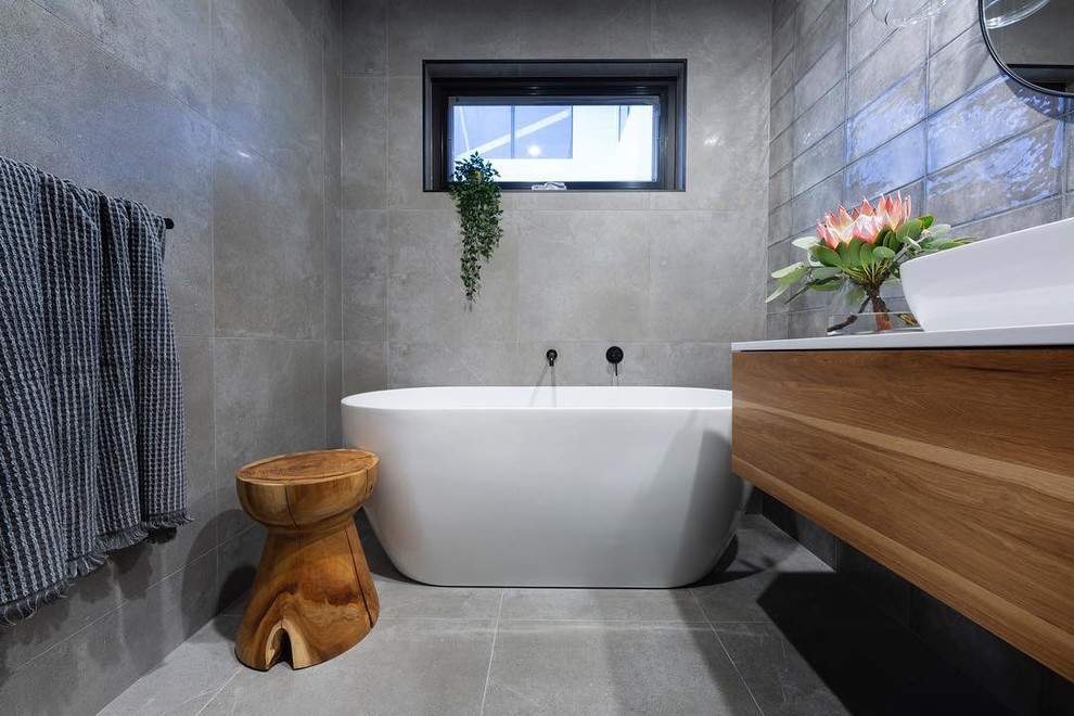 Inspiration for a mid-sized contemporary bathroom in Canberra - Queanbeyan with flat-panel cabinets, medium wood cabinets, a freestanding tub, gray tile, a vessel sink, grey floor and white benchtops.