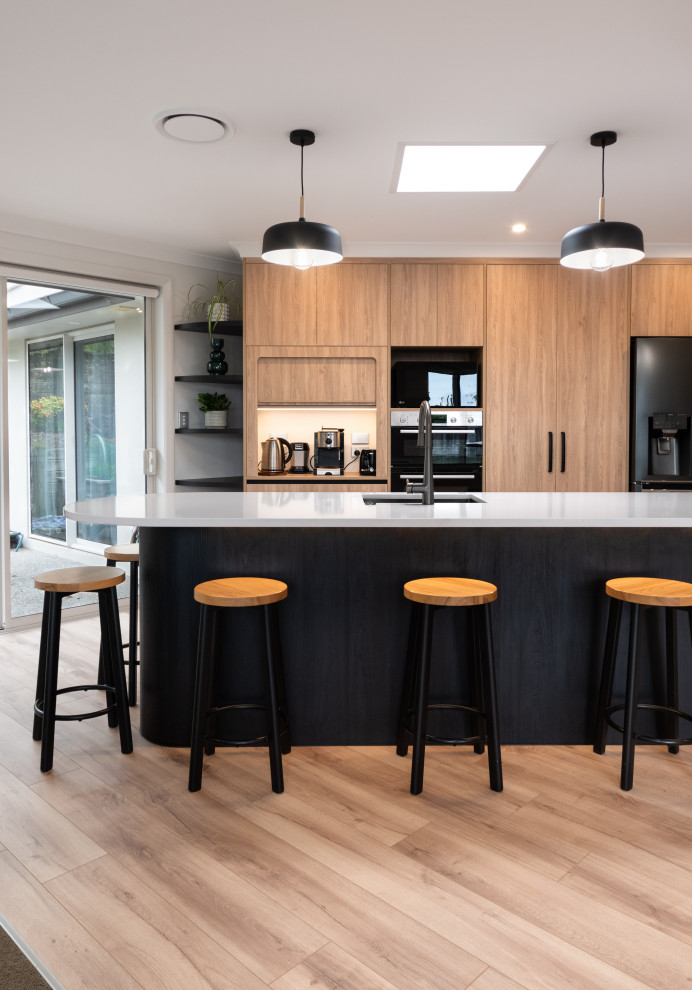 Mid-sized modern eat-in kitchen in Other with an undermount sink, light wood cabinets, quartz benchtops, black appliances, laminate floors, with island and white benchtop.
