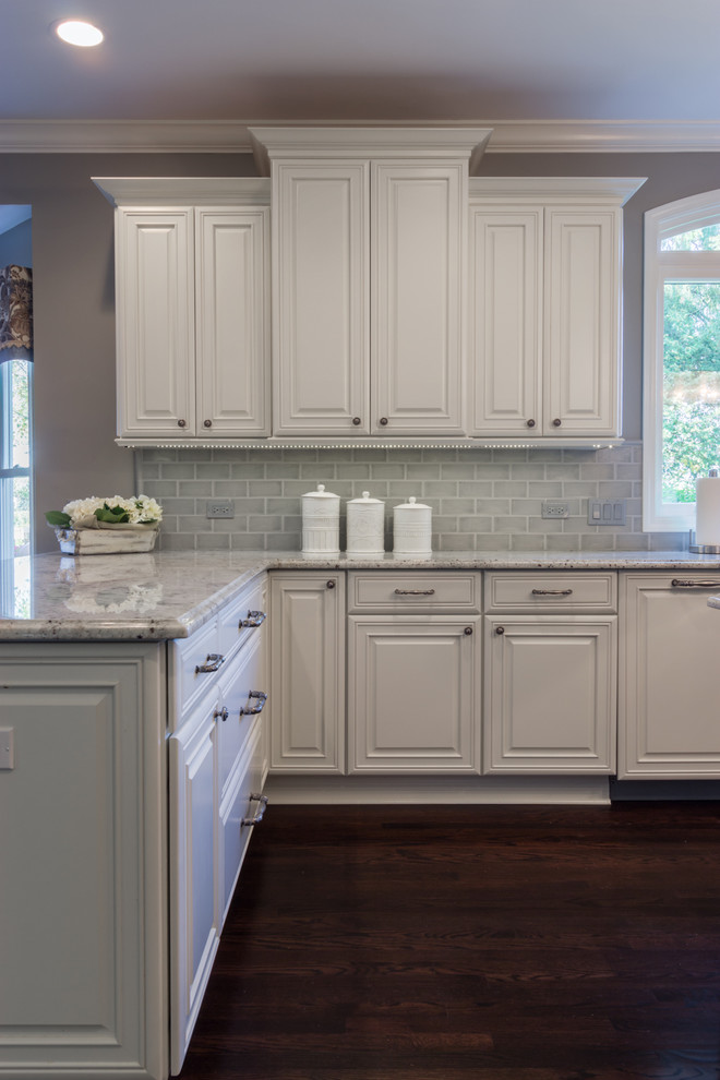 Large transitional u-shaped dark wood floor kitchen photo in Chicago with a double-bowl sink, raised-panel cabinets, white cabinets, granite countertops, gray backsplash, subway tile backsplash, stainless steel appliances and an island