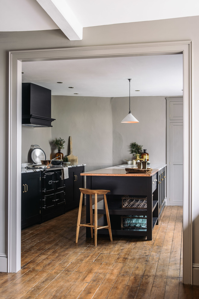Photo of a mid-sized country single-wall open plan kitchen in Other with an integrated sink, shaker cabinets, black cabinets, copper benchtops, grey splashback, black appliances, medium hardwood floors and with island.