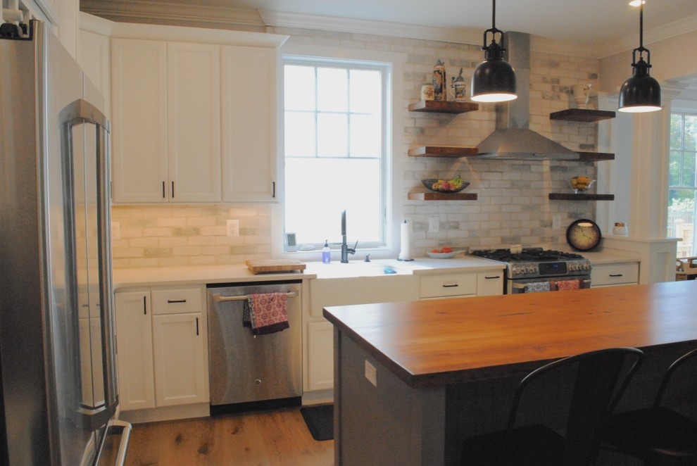 Eat-in kitchen - transitional light wood floor eat-in kitchen idea in Baltimore with a farmhouse sink, flat-panel cabinets, white cabinets, quartz countertops, white backsplash, stone tile backsplash, stainless steel appliances and an island