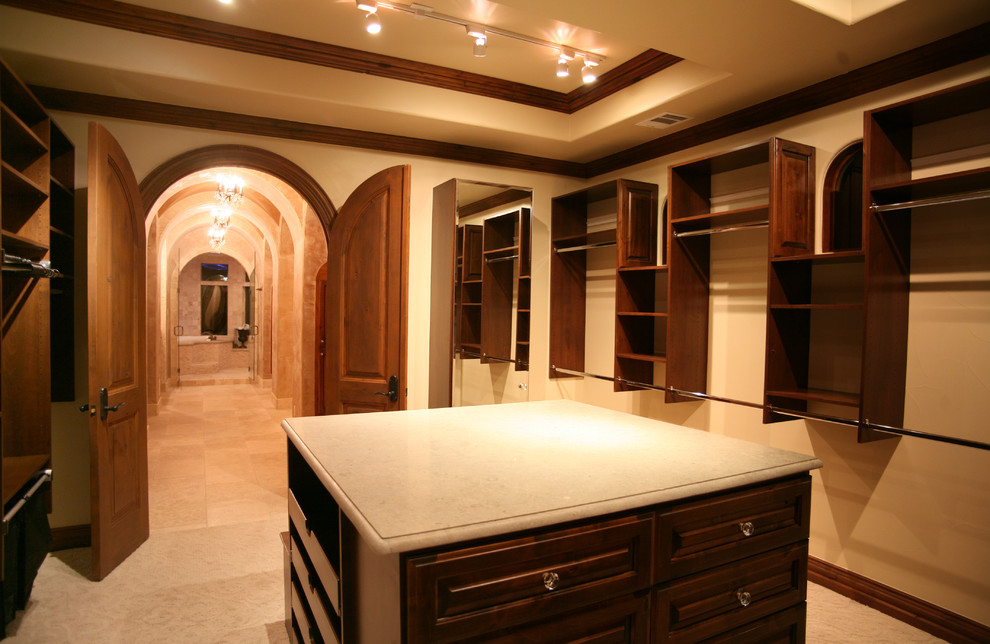This is an example of a large mediterranean gender-neutral dressing room in Austin with raised-panel cabinets, dark wood cabinets and carpet.