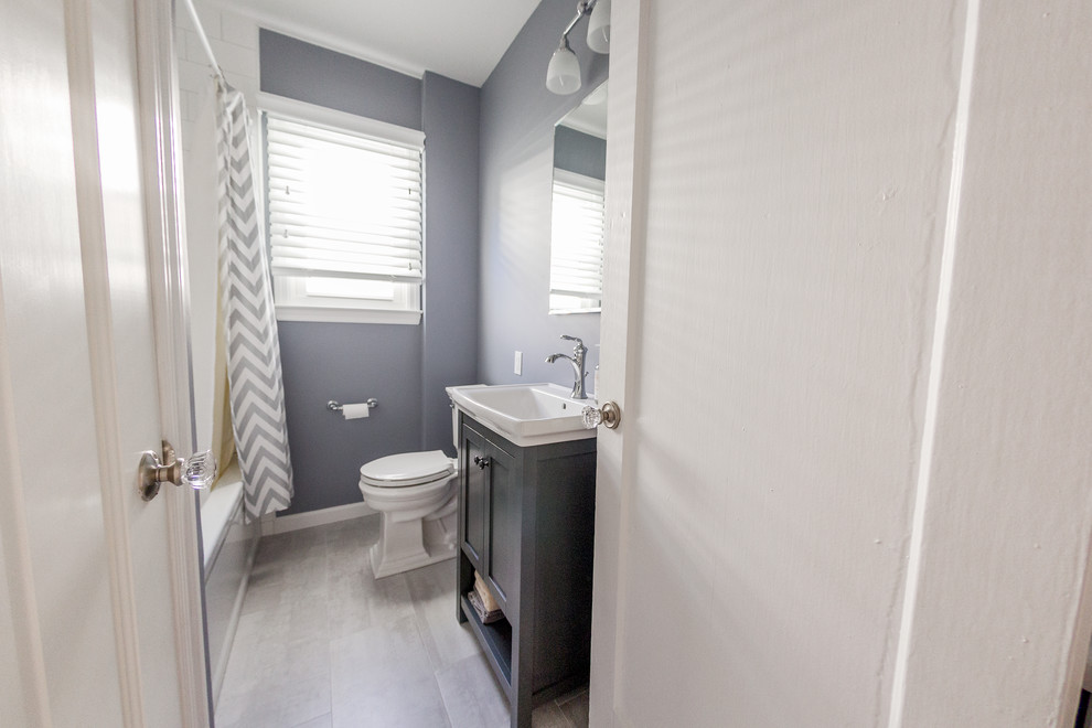 Small contemporary bathroom in New York with a drop-in sink, recessed-panel cabinets, grey cabinets, solid surface benchtops, an alcove tub, an alcove shower, a one-piece toilet, white tile, porcelain tile, grey walls and porcelain floors.