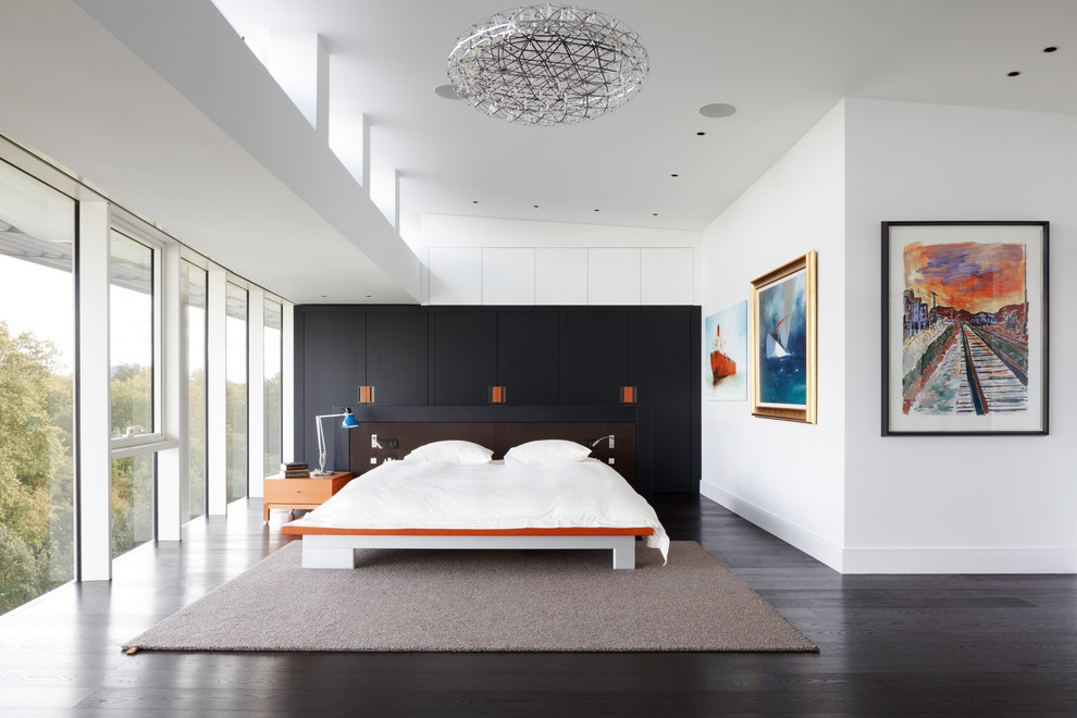 Design ideas for an expansive contemporary master bedroom in London with white walls, dark hardwood floors and no fireplace.