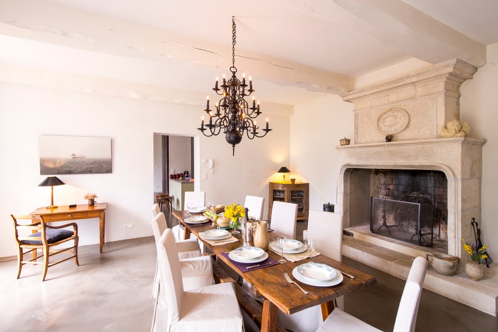 Large country separate dining room in London with white walls, concrete floors, a standard fireplace and a stone fireplace surround.