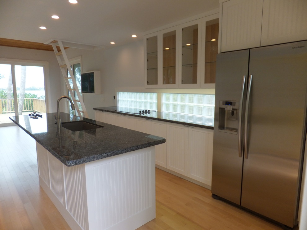 Inspiration for a mid-sized beach style galley separate kitchen in Orlando with an undermount sink, beaded inset cabinets, white cabinets, granite benchtops, glass tile splashback, stainless steel appliances, light hardwood floors, with island and brown floor.