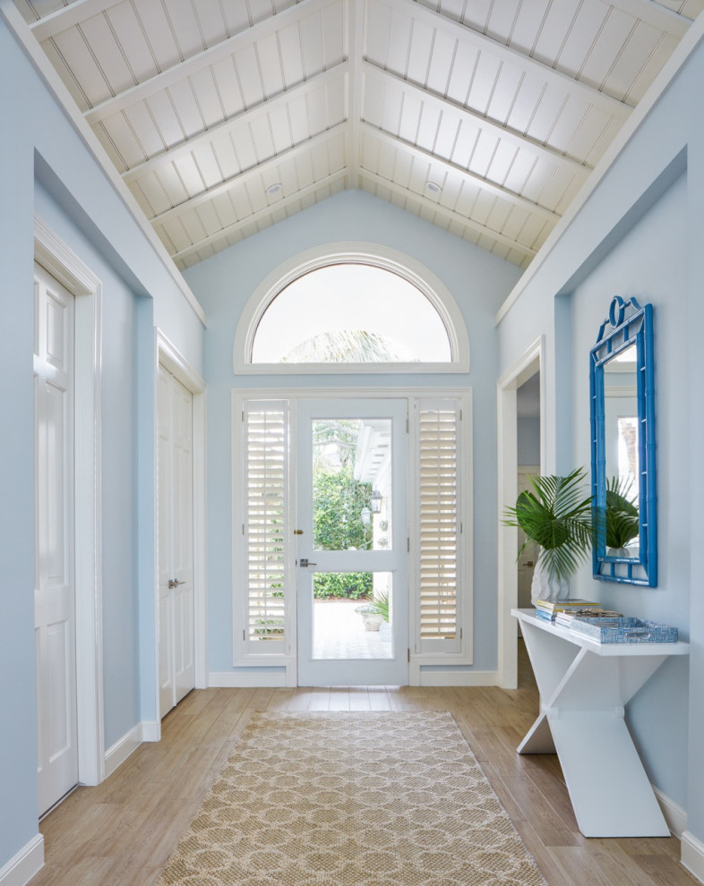 Réalisation d'une entrée marine avec un mur bleu, une porte en verre, un sol beige et un plafond en lambris de bois.