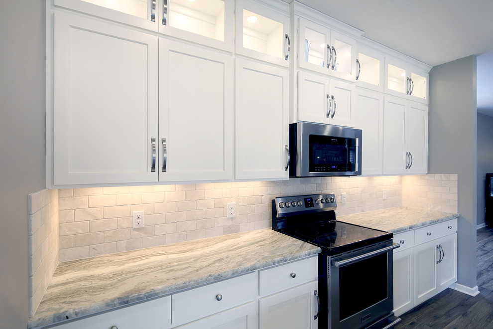 Transitional l-shaped gray floor eat-in kitchen photo with an undermount sink, glass-front cabinets, white cabinets, stainless steel appliances, an island, beige backsplash, stone tile backsplash and multicolored countertops