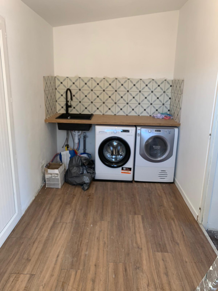 Mid-sized modern dedicated laundry room in Toulouse with wood benchtops, multi-coloured splashback, ceramic splashback, laminate floors, a side-by-side washer and dryer, brown floor and brown benchtop.