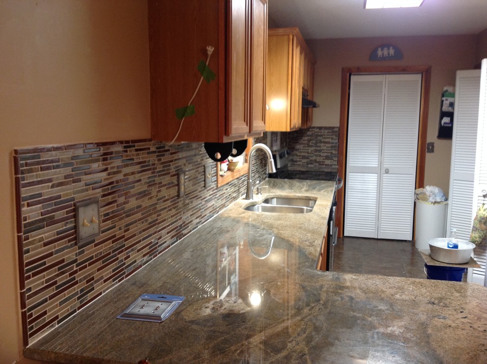 Example of a l-shaped eat-in kitchen design with an undermount sink, flat-panel cabinets, brown backsplash, glass tile backsplash, stainless steel appliances and a peninsula