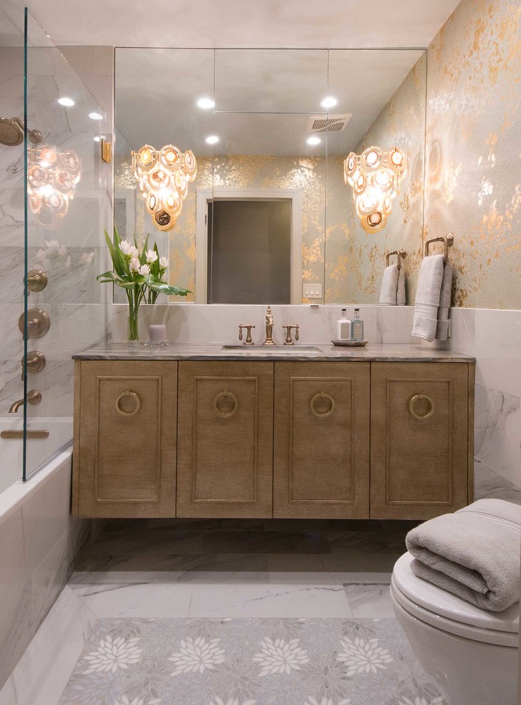 This is an example of a mid-sized traditional master bathroom in New York with furniture-like cabinets, beige cabinets, a corner tub, a shower/bathtub combo, a two-piece toilet, gray tile, porcelain tile, multi-coloured walls, porcelain floors, an undermount sink, grey floor and a hinged shower door.