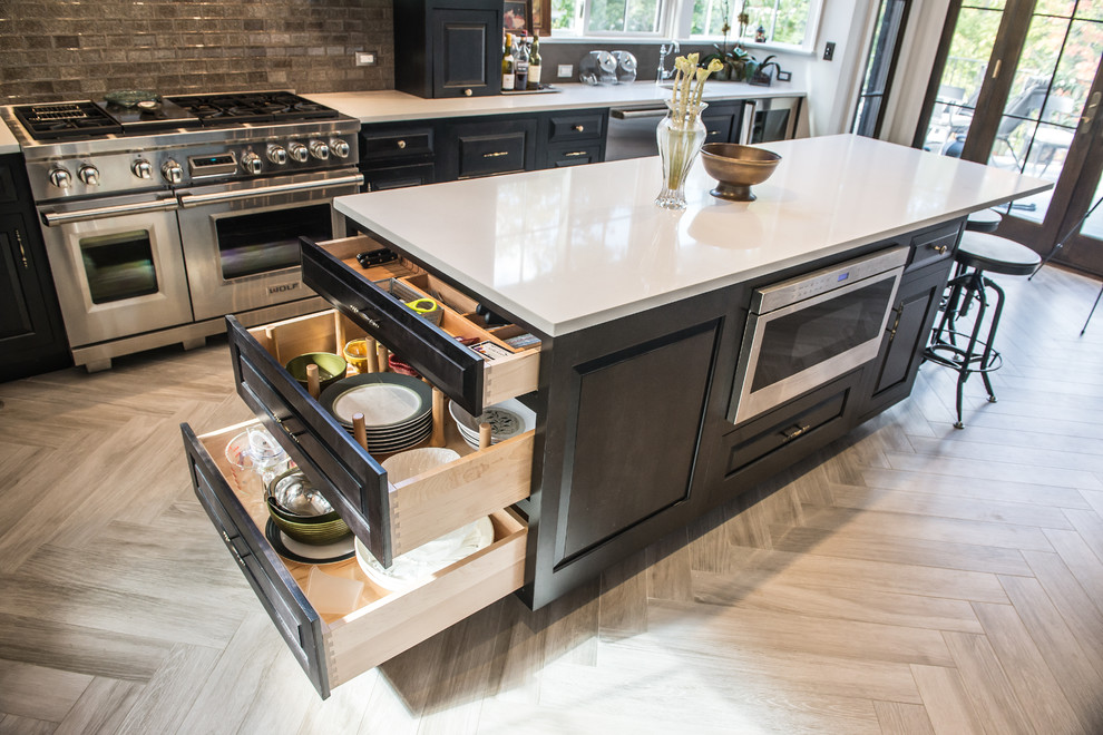 Large transitional u-shaped eat-in kitchen in New York with raised-panel cabinets, black cabinets, stainless steel appliances, with island, an undermount sink, solid surface benchtops, grey splashback, ceramic splashback and porcelain floors.