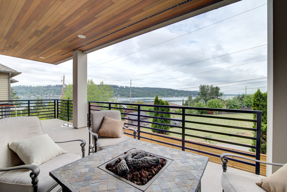 This is an example of a large contemporary backyard deck in Seattle with a fire feature and a roof extension.