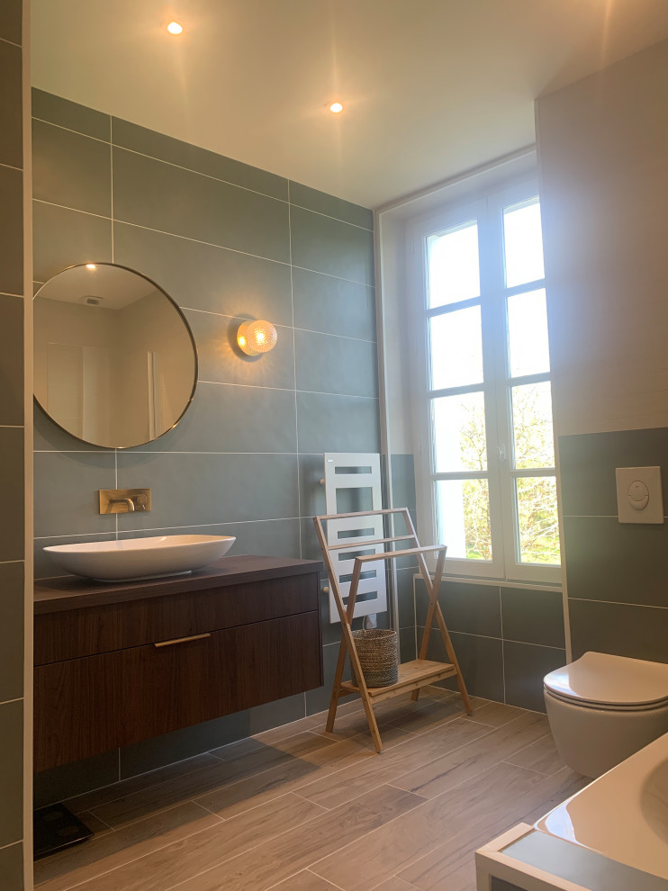 Свежая идея для дизайна: ванная комната среднего размера в современном стиле с плоскими фасадами, темными деревянными фасадами, полновстраиваемой ванной, угловым душем, инсталляцией, зеленой плиткой, керамической плиткой, зелеными стенами, полом из плитки под дерево, настольной раковиной, столешницей из ламината, коричневым полом, душем с раздвижными дверями, разноцветной столешницей и тумбой под одну раковину - отличное фото интерьера