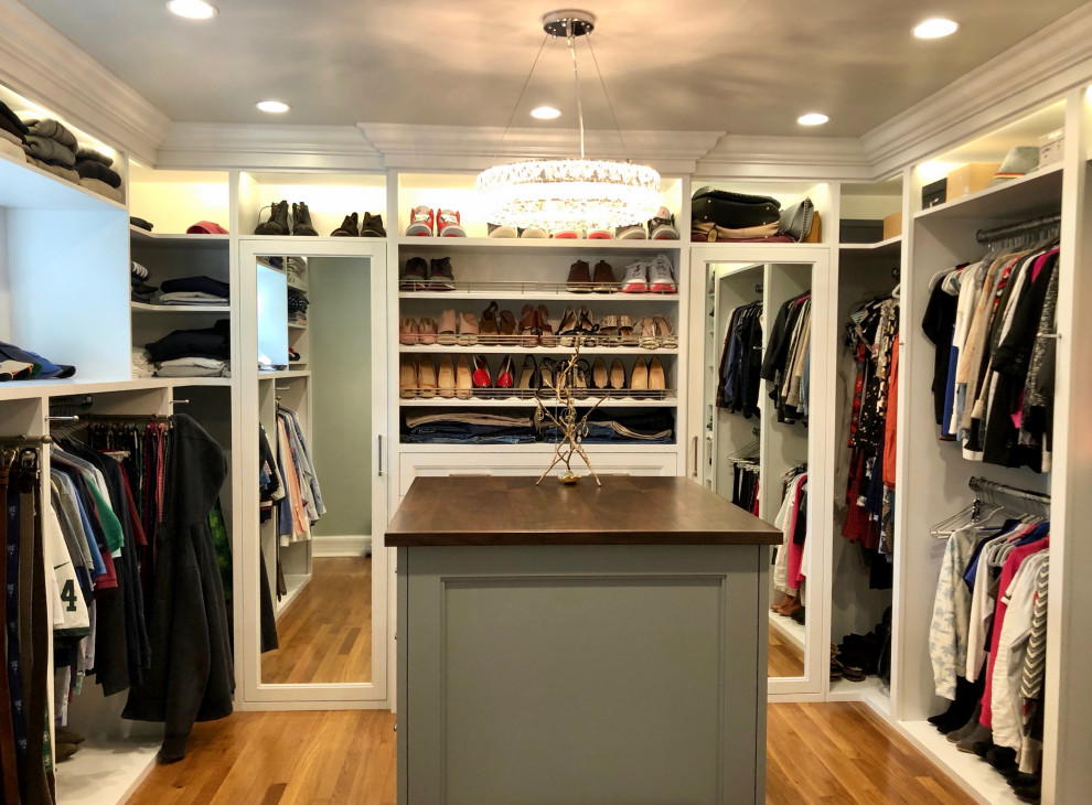 Large classic gender neutral walk-in wardrobe in New York with open cabinets, yellow cabinets, medium hardwood flooring and brown floors.