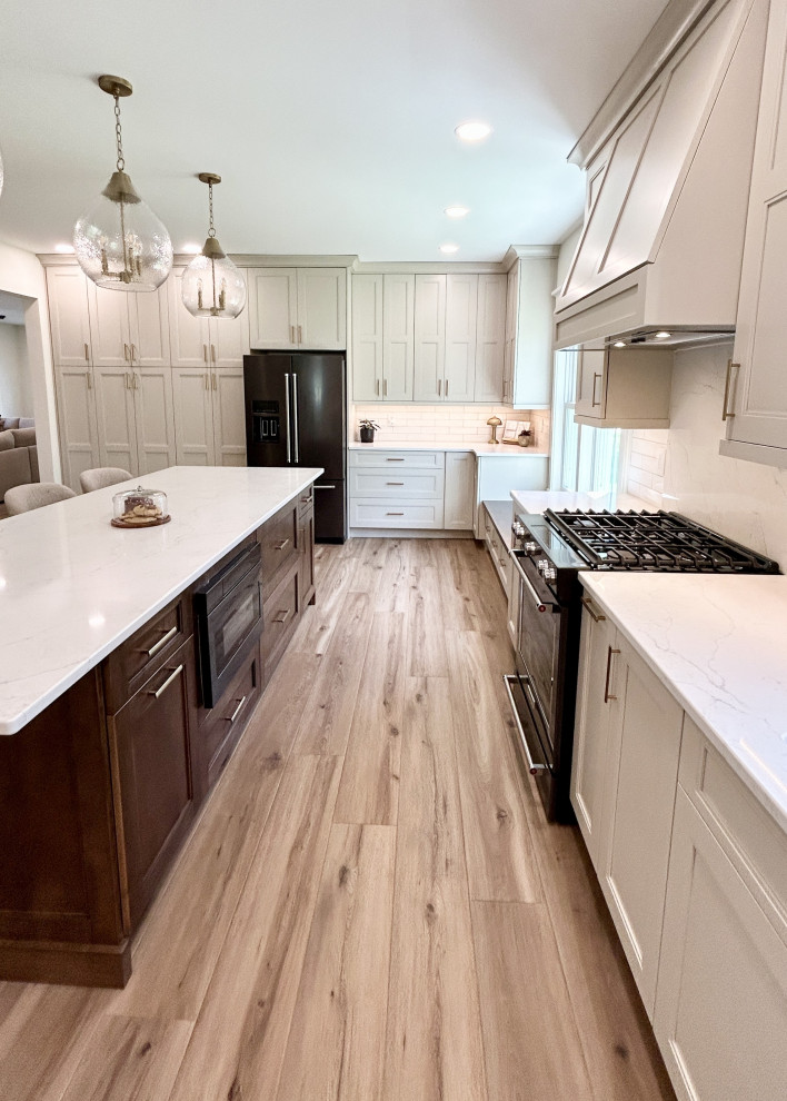Inspiration for a large transitional u-shaped light wood floor open concept kitchen remodel with an undermount sink, flat-panel cabinets, white cabinets, quartz countertops, white backsplash, ceramic backsplash, black appliances, an island and white countertops