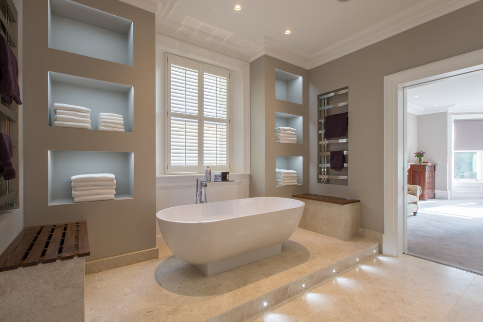 Photo of a large contemporary master bathroom in London with flat-panel cabinets, dark wood cabinets, a freestanding tub, an open shower, a wall-mount toilet, beige tile, stone slab, beige walls, marble floors, an integrated sink and glass benchtops.