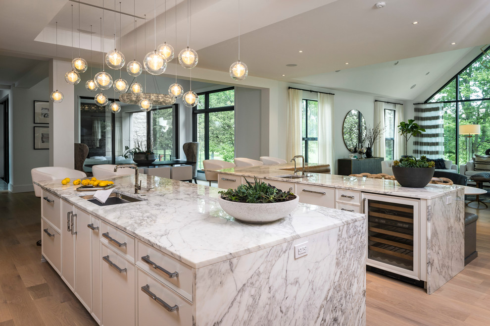 Design ideas for an expansive contemporary l-shaped open plan kitchen in Indianapolis with an undermount sink, flat-panel cabinets, white cabinets, marble benchtops, white splashback, porcelain splashback, stainless steel appliances, medium hardwood floors, multiple islands and brown floor.