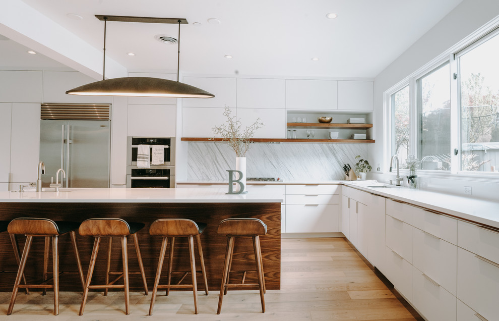 Design ideas for a contemporary l-shaped kitchen in Seattle with an undermount sink, flat-panel cabinets, white cabinets, white splashback, stainless steel appliances, medium hardwood floors, with island, brown floor and white benchtop.