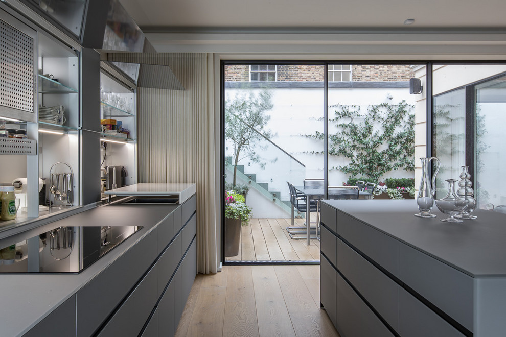 This is an example of a mid-sized modern galley eat-in kitchen in London with glass-front cabinets, grey cabinets, glass benchtops, white splashback, glass sheet splashback, with island and grey benchtop.