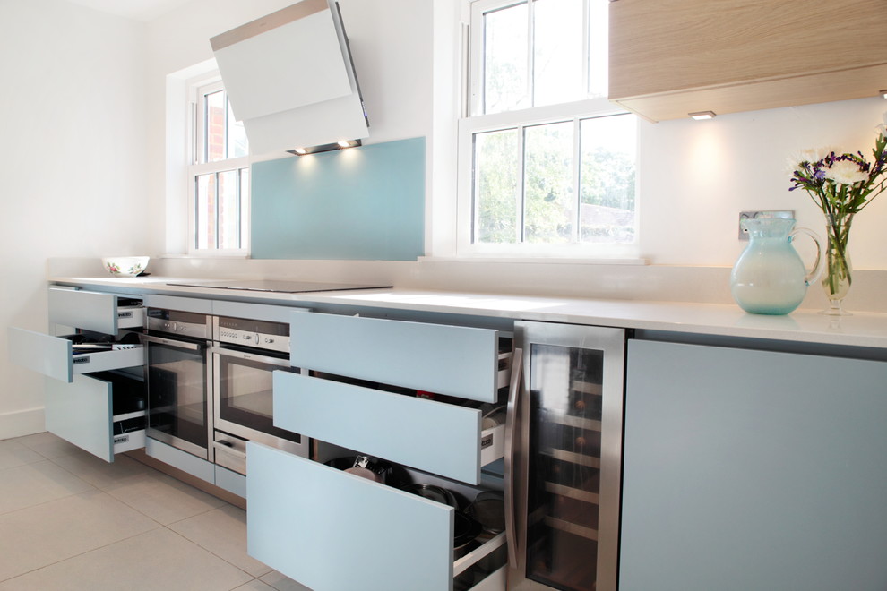 Mid-sized contemporary single-wall eat-in kitchen in Buckinghamshire with an undermount sink, flat-panel cabinets, blue cabinets, quartzite benchtops, blue splashback, glass sheet splashback, stainless steel appliances, porcelain floors and with island.