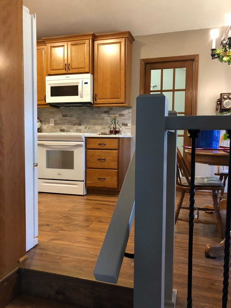Inspiration for a mid-sized transitional u-shaped laminate floor and brown floor eat-in kitchen remodel in Omaha with an undermount sink, raised-panel cabinets, medium tone wood cabinets, quartz countertops, beige backsplash, stone tile backsplash, white appliances and white countertops