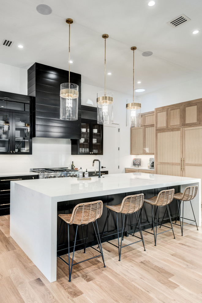 Design ideas for an expansive transitional l-shaped open plan kitchen in Dallas with a farmhouse sink, recessed-panel cabinets, black cabinets, quartz benchtops, white splashback, marble splashback, stainless steel appliances, light hardwood floors, with island, brown floor and white benchtop.
