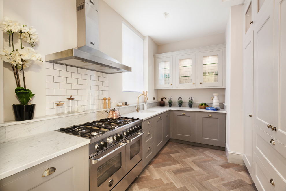 Photo of a small transitional l-shaped kitchen in London with a single-bowl sink, glass-front cabinets, white cabinets, white splashback, subway tile splashback, stainless steel appliances, medium hardwood floors and no island.