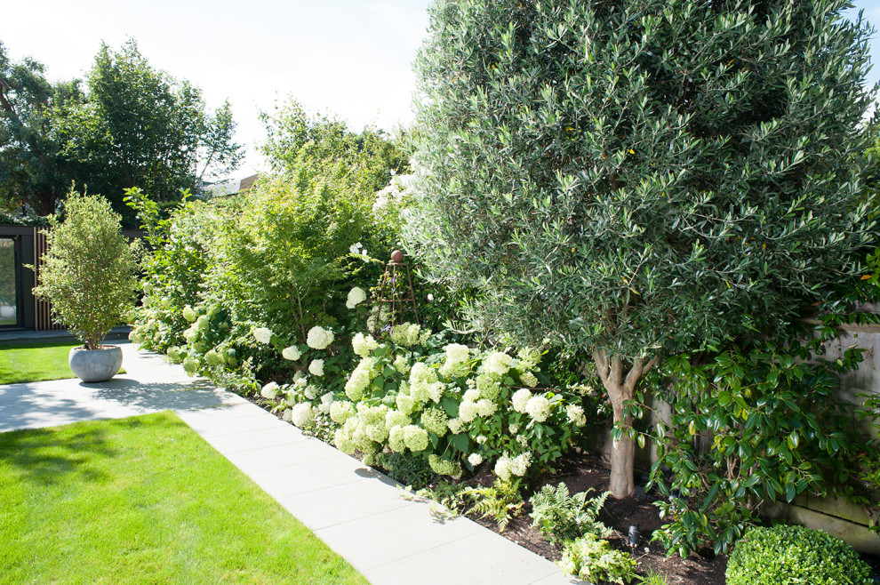 На фото: большой солнечный, летний регулярный сад на заднем дворе в современном стиле с клумбами, хорошей освещенностью, покрытием из каменной брусчатки и с деревянным забором с
