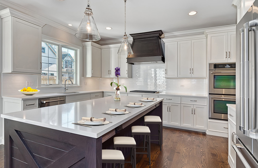 This is an example of a large transitional u-shaped separate kitchen in Chicago with an undermount sink, shaker cabinets, white cabinets, white splashback, subway tile splashback, stainless steel appliances, medium hardwood floors, with island and granite benchtops.