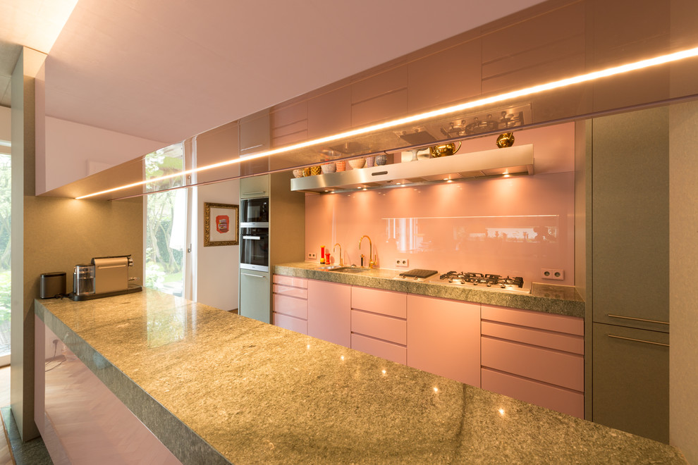 Photo of a mid-sized midcentury galley open plan kitchen in Other with a single-bowl sink, flat-panel cabinets, granite benchtops, pink splashback, glass sheet splashback, with island and grey floor.