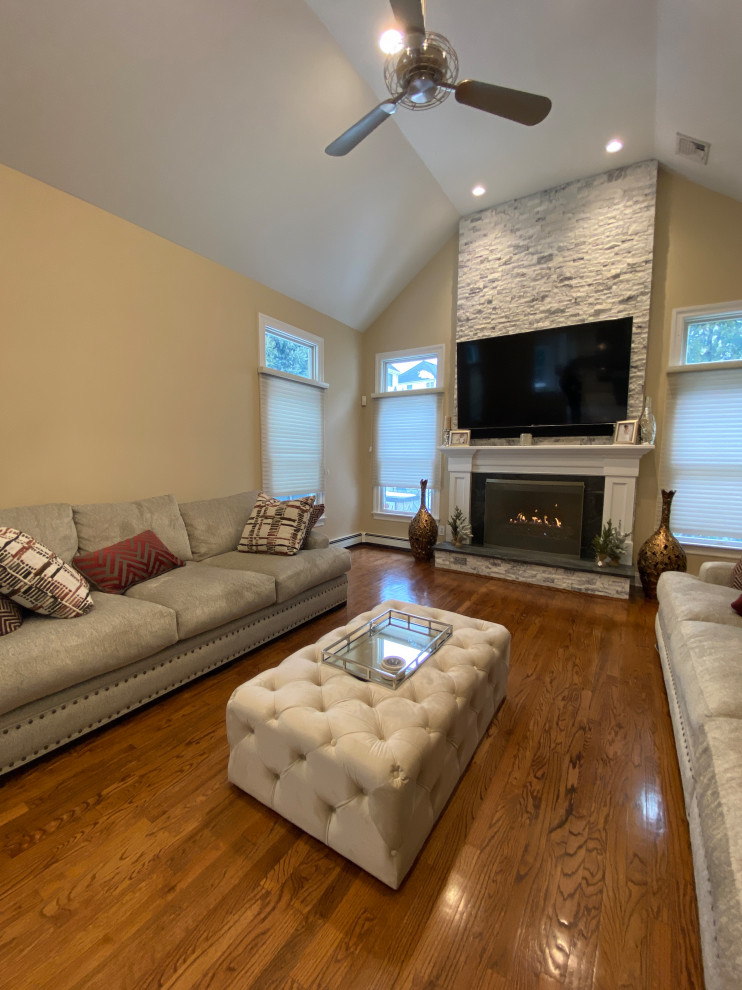 Offenes Eklektisches Wohnzimmer mit beiger Wandfarbe, braunem Holzboden, Kamin, Kaminumrandung aus gestapelten Steinen, TV-Wand und gewölbter Decke in New York