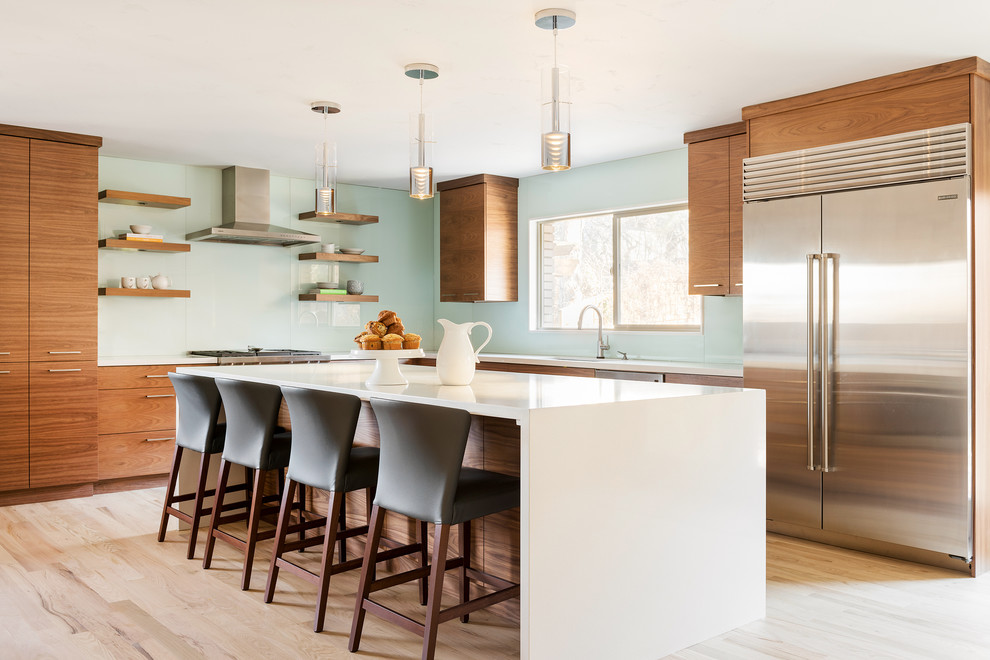 Contemporary l-shaped kitchen in Salt Lake City with flat-panel cabinets, medium wood cabinets, blue splashback, glass sheet splashback, stainless steel appliances, light hardwood floors, with island, beige floor and white benchtop.