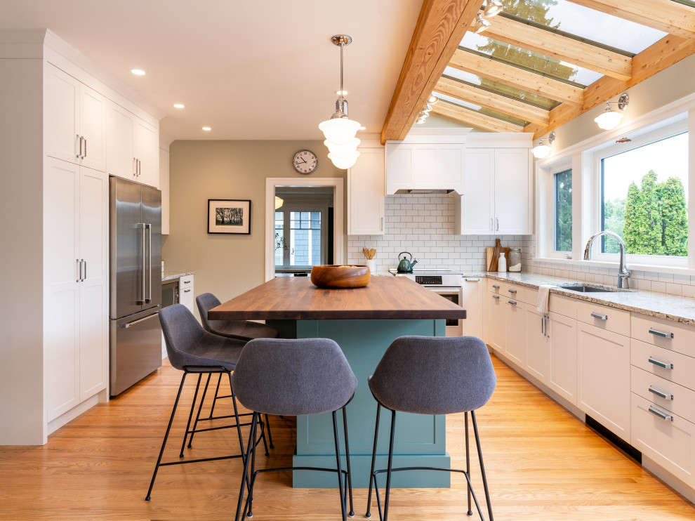 Photo of a transitional u-shaped kitchen in Vancouver with an undermount sink, shaker cabinets, white cabinets, white splashback, subway tile splashback, stainless steel appliances, medium hardwood floors, with island, brown floor, grey benchtop, exposed beam and vaulted.